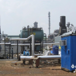 A blue container with pipes in front of a blue building, showcasing industrial architecture.