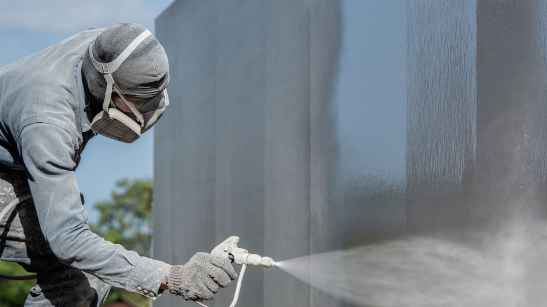 Worker spray-applying epoxy coating on steel panels showing industrial surface protection 